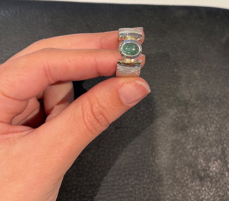 Op de afbeelding: Een zilveren ring met een groene edelsteen in een getextureerde band.