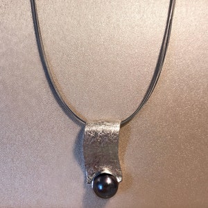 May include: A silver necklace with a textured pendant and a dark gray pearl.