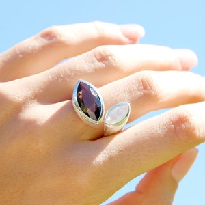 May include: A silver ring with two marquise-shaped gemstones. The larger stone is a dark brown smoky quartz, and the smaller stone is a white moonstone. The ring is designed to wrap around the finger.