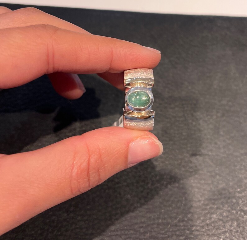 Op de afbeelding: Een zilveren ring met een groene ovale edelsteen in het midden. De ring heeft een getextureerde band.