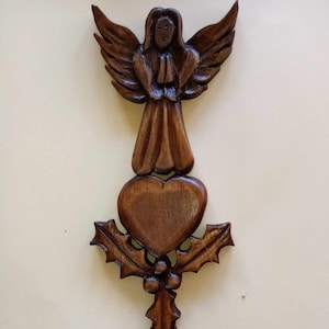 May include: A wooden spoon carved with an angel holding a heart and holly leaves. The spoon is brown and has a natural wood finish.