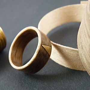 Puede incluir: Un anillo de madera con una incrustación de triángulo de oro. El anillo está hecho de madera oscura y tiene un acabado natural. El triángulo de oro está incrustado en la madera y es un oro brillante y brillante.