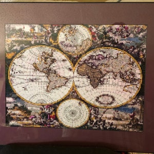 May include: A framed diamond painting depicting a vintage world map with four circular sections. The map is surrounded by a decorative border with gold accents.