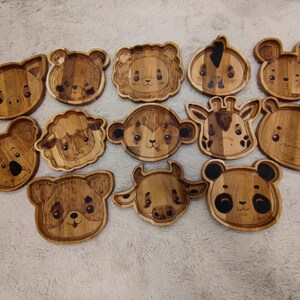 May include: Set of 12 wooden plates featuring various animal designs. Each plate is hand-painted with a unique animal face, including a pig, koala, sheep, monkey, giraffe, hippo, panda, lion, mouse, and a few others.