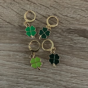 May include: Four gold-colored earrings with four-leaf clover charms. Two charms are green, one is light green, and one is dark green.