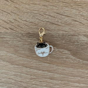 Peut inclure: Breloque en or représentant un chat noir qui sort d'une tasse à café blanche avec le mot "café" écrit sur le côté.
