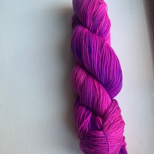 May include: A skein of hand-dyed yarn in shades of pink and purple. The yarn is tightly wound and has a gradient effect, transitioning from a deep magenta to a lighter pink. The yarn is likely made of wool or a similar fiber, suitable for knitting or crochet projects.