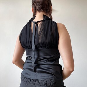 May include: Black halter top with a satin bodice and a sheer, ruffled neckline. The top features a tie closure at the back and a gathered, ruffled hem. The design is sleeveless and has a vintage aesthetic.