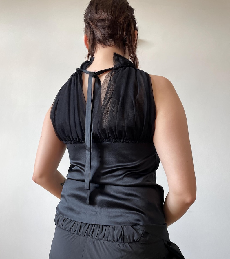 May include: Black halter top with a satin bodice and a sheer, ruffled neckline. The top features a tie closure at the back and a gathered, ruffled hem. The design is sleeveless and has a vintage aesthetic.