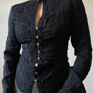 May include: Black long-sleeve blouse with a high collar and gold buttons. The blouse features vertical textured stripes and a slight sparkle throughout the fabric. The sleeves have a flared design at the wrist, and the blouse is buttoned down the front.