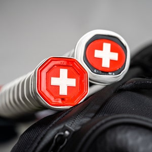 May include: Two silver tennis rackets with red and white Swiss cross logos on the handles.