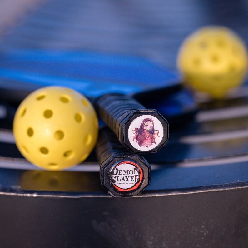 May include: Two black pickleball paddles with custom grip tape. One paddle has a Demon Slayer logo and the other has an anime character from the show.