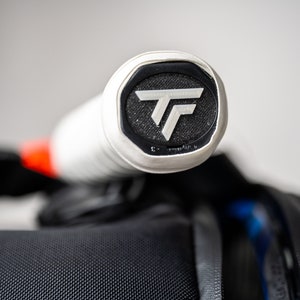 May include: Close-up of the end of a white tennis racket handle with a black and white logo that says "TF".