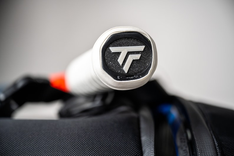 May include: Close-up of the end of a white tennis racket handle with a black and white logo that says "TF".
