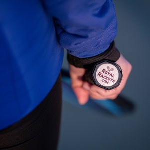 May include: A person is holding a black tennis racket with a white sticker on the end. The sticker says "Royal Rackets .com" and has a tennis racket icon.