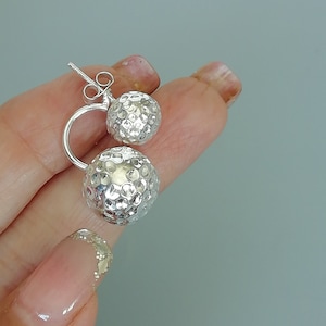 Puede incluir: Pendientes de plata con dos bolas redondas texturizadas conectadas por una barra curva.