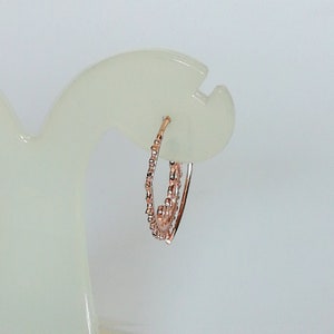 May include: A pair of rose gold hoop earrings with a textured design. The earrings are on a white display stand.