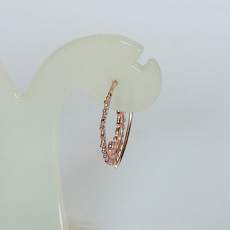 May include: A pair of rose gold hoop earrings with a textured design. The earrings are on a white display stand.