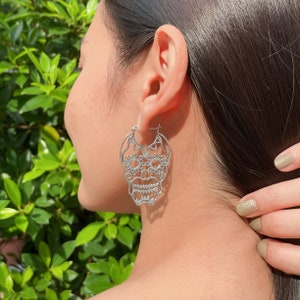 May include: Silver hoop earrings with a detailed sugar skull design.