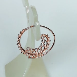May include: Rose gold hoop earrings with a delicate, swirling design. The earrings are made of metal and have a circular shape.