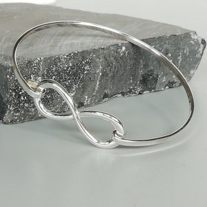 Könnte beinhalten: Silberner Unendlichkeits-Armband. Das Armband ist aus poliertem Silber gefertigt und hat ein schlichtes Unendlichkeits-Symbol.