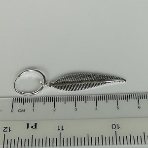 Puede incluir: Pendiente de aro de plata con un dije de pluma. El pendiente mide aproximadamente 5 cm de largo.