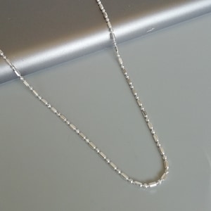 May include: A silver chain necklace with a delicate, round link design. The chain is made of small, evenly spaced, round links.