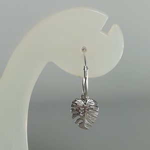 May include: Silver hoop earrings with a small, detailed leaf charm hanging from the bottom.