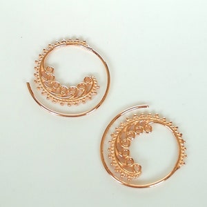 May include: A pair of gold-toned spiral hoop earrings with a delicate floral design.