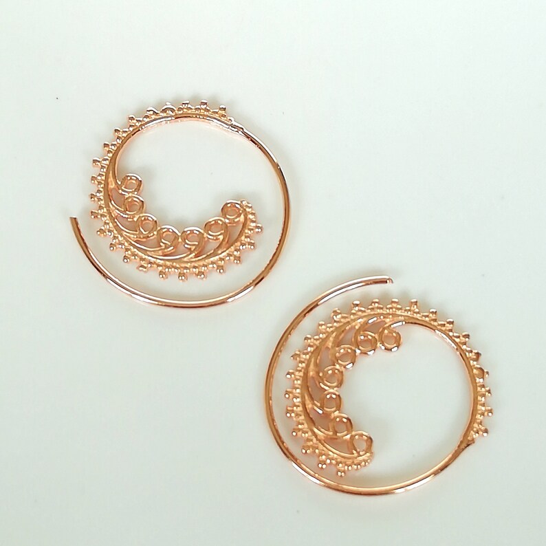 May include: A pair of gold-toned spiral hoop earrings with a delicate floral design.