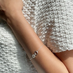 May include: A silver infinity bracelet with a heart charm. The bracelet is on a person's wrist.