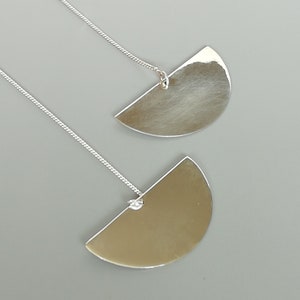 Puede incluir: Un par de pendientes de plata con un diseño de medio círculo. Los pendientes están suspendidos de una delicada cadena de plata.