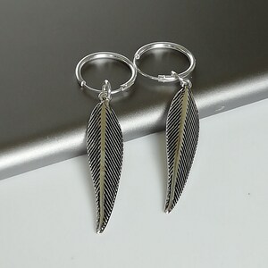 Puede incluir: Un par de pendientes de aro de plata con colgantes en forma de pluma. Los pendientes son simples y elegantes, y las plumas a&ntilde;aden un toque de fantas&iacute;a.