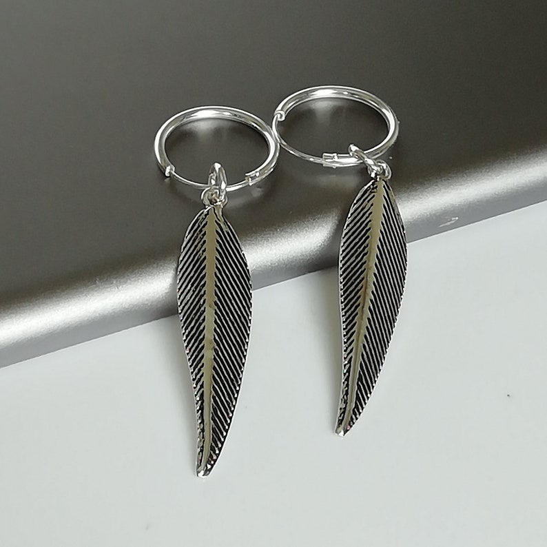 Puede incluir: Un par de pendientes de aro de plata con colgantes en forma de pluma. Los pendientes son simples y elegantes, y las plumas a&ntilde;aden un toque de fantas&iacute;a.