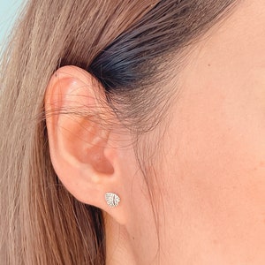 May include: A close-up of a person's ear with a small silver earring in the shape of a leaf.