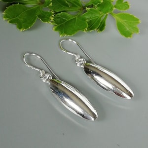 May include: A pair of silver dangle earrings with a smooth, oval-shaped pendant. The earrings have a simple, elegant design.