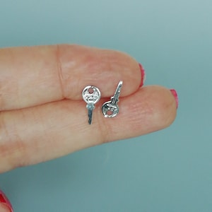 Peut inclure: Une paire de boucles d'oreilles clous en argent en forme de clé. Les boucles d'oreilles sont petites et délicates, et elles feraient un excellent cadeau pour un ami ou un être cher.