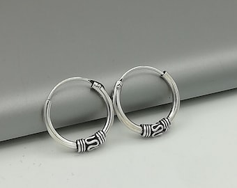 May include: A pair of silver hoop earrings with a decorative design on the front. The earrings are simple and elegant.