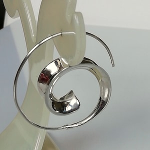 May include: Silver hoop earrings with a spiral design. The earrings are made of a thin metal wire and have a simple, modern look.