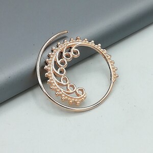 May include: A gold-toned hoop earring with a delicate, intricate design featuring a crescent moon shape with a floral pattern. The earring is made of metal and has a smooth, polished finish.