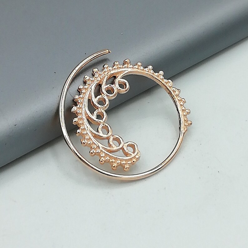 May include: A gold-toned hoop earring with a delicate, intricate design featuring a crescent moon shape with a floral pattern. The earring is made of metal and has a smooth, polished finish.