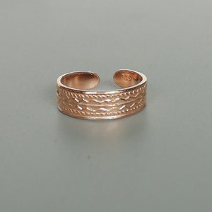 Könnte beinhalten: Ein Zehenring aus Roségold mit einem geflochtenen Design. Der Ring ist verstellbar und hat eine Größe von 28.