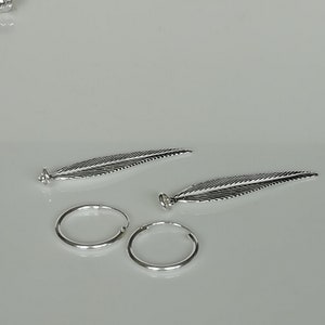Puede incluir: Dos pendientes de plata con forma de pluma y cierre de aro. Las plumas tienen detalles de l&iacute;neas y un acabado plateado.