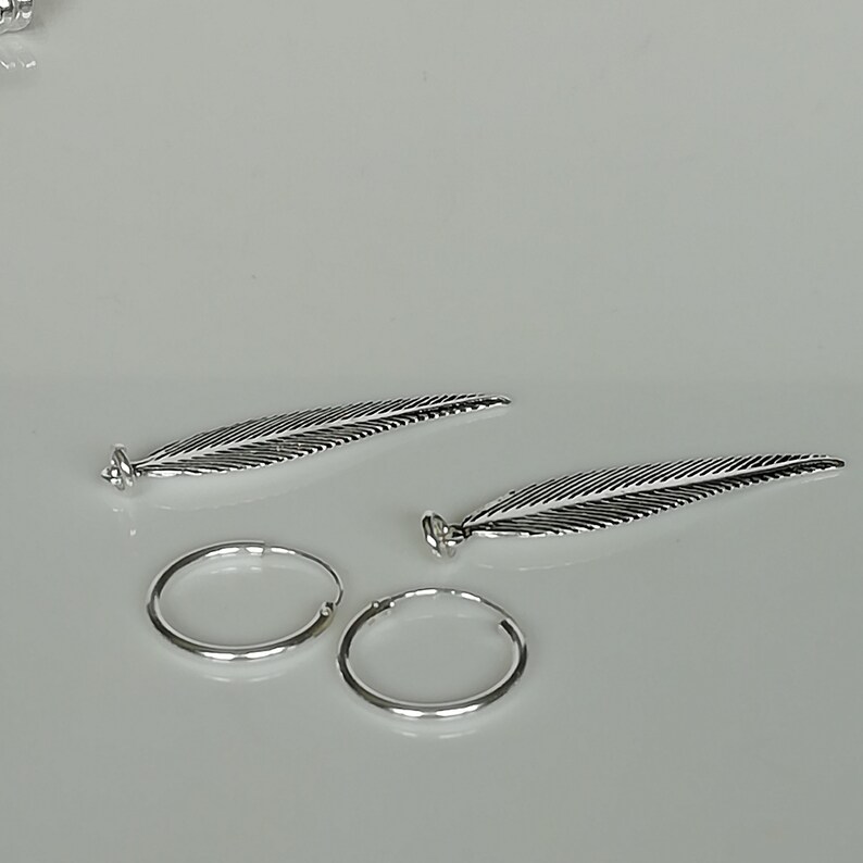 Puede incluir: Dos pendientes de plata con forma de pluma y cierre de aro. Las plumas tienen detalles de l&iacute;neas y un acabado plateado.