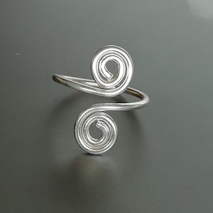 Könnte beinhalten: Silberring mit zwei Spiralmotiven. Der Ring ist aus Draht gefertigt und verstellbar.