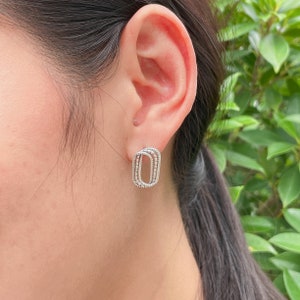 Könnte beinhalten: Silberne Ohrringe mit geometrischem Design. Die Ohrringe sind oval geformt und haben eine strukturierte Oberfläche.