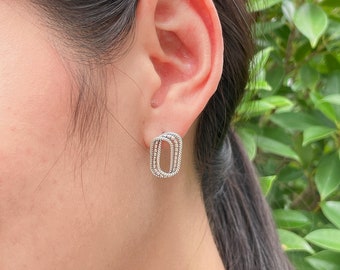 May include: Silver earrings with a geometric design. The earrings are oval shaped and have a textured surface.