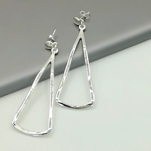 May include: A pair of silver dangle earrings with a triangle shape. The earrings have a textured surface and a simple design.