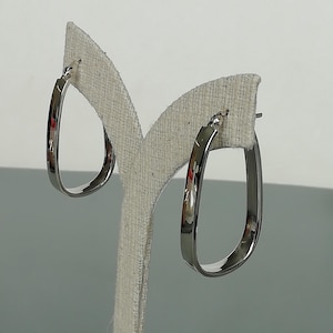 May include: A pair of silver oval hoop earrings. The earrings are on a white display stand.