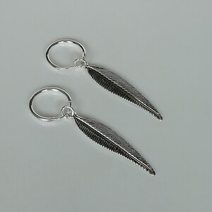 Puede incluir: Un par de pendientes de aro de plata con colgantes de plumas. Las plumas tienen un dise&ntilde;o texturizado.